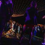 Wedding reception at private residence with twinkle light display over black dance floor. Pattern wash over dance floor and band in foreground lit in purple.